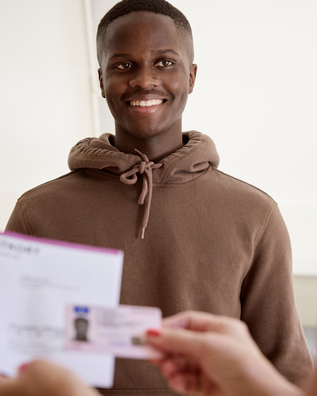 Smiling young man showing identification documents to a person across the counter